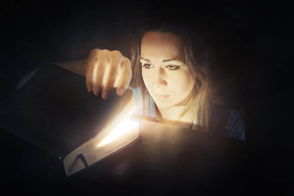 A woman looks inside a Bible that is glowing