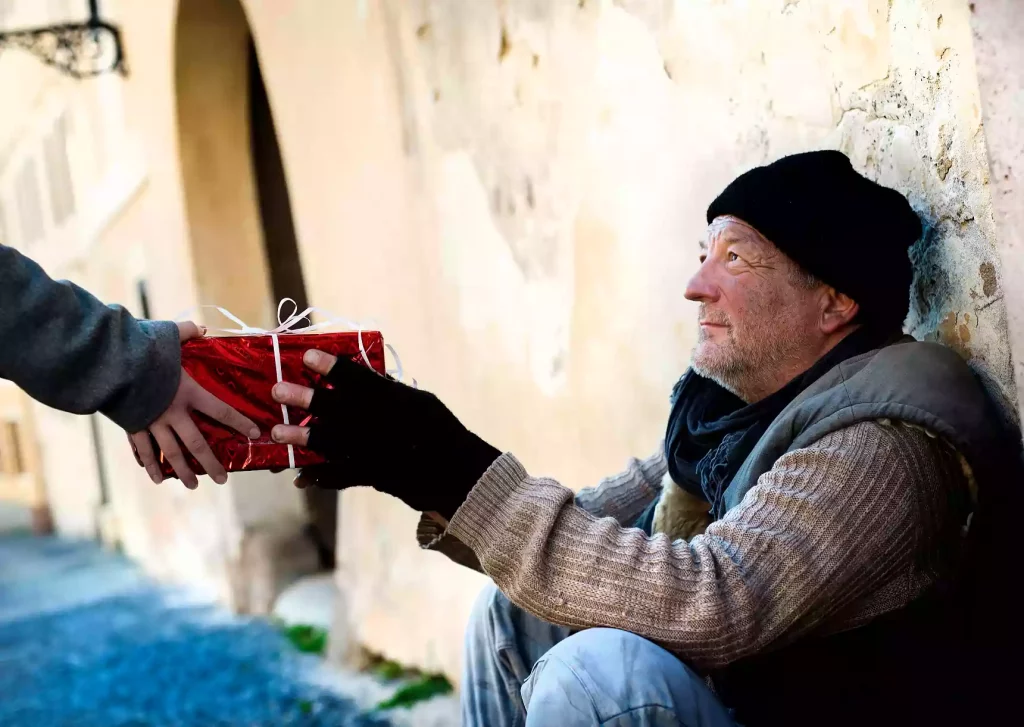 A homeless man sits on the ground receiving a present rapped in red paper.