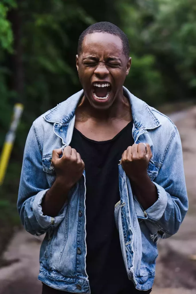 Black African man raising his fists to his chest screaming with closed eyes. 