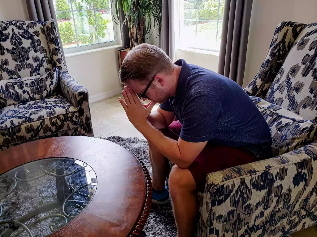 A man sitting on chair with his elbows resting on his knees and his forehead resting on his hands