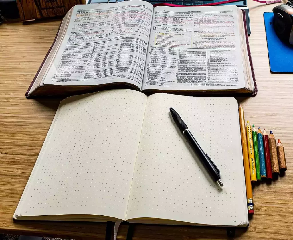 An open Bible and open journal laying on a desk.