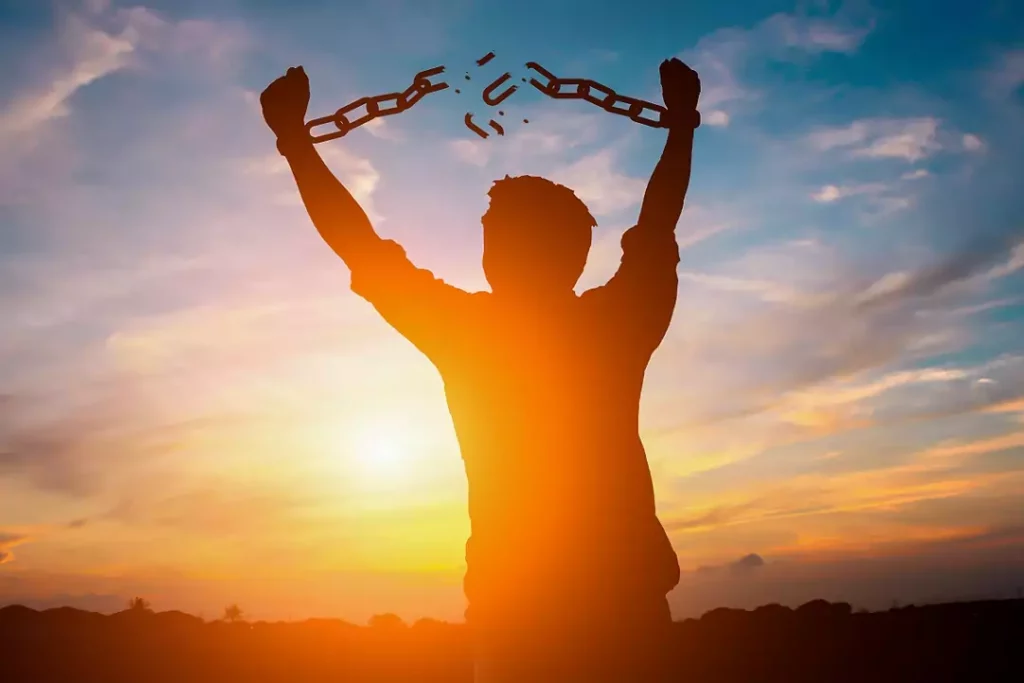 a person breaking their chains above their head in front of a sun set